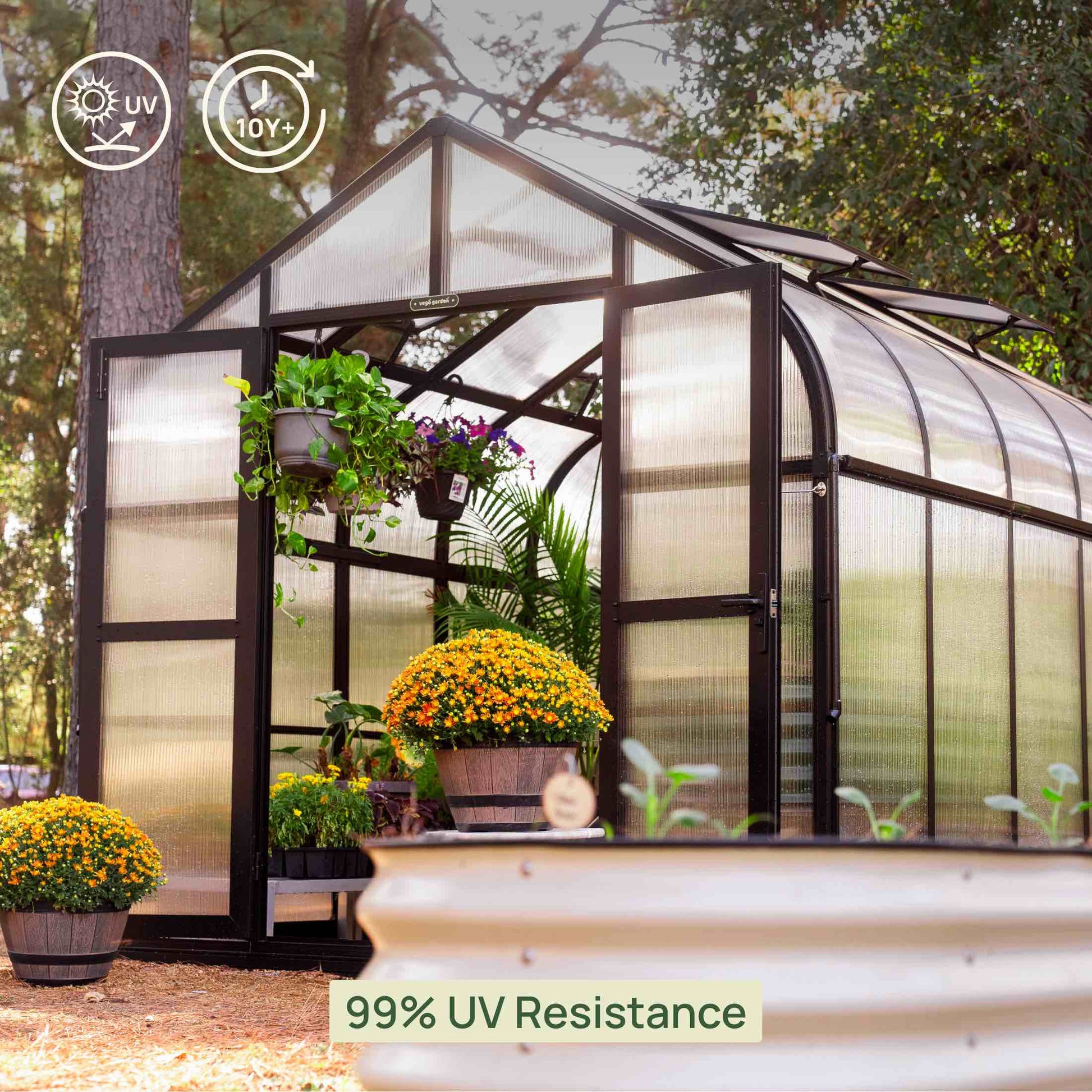 8.5ft wide green metal greenhouse with double doors and clear panels set on a gravel path in a sunny garden