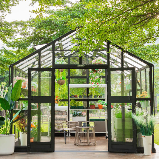 Victorian-style green greenhouse with tall glass panes and ornate metal framing on a gravel garden path